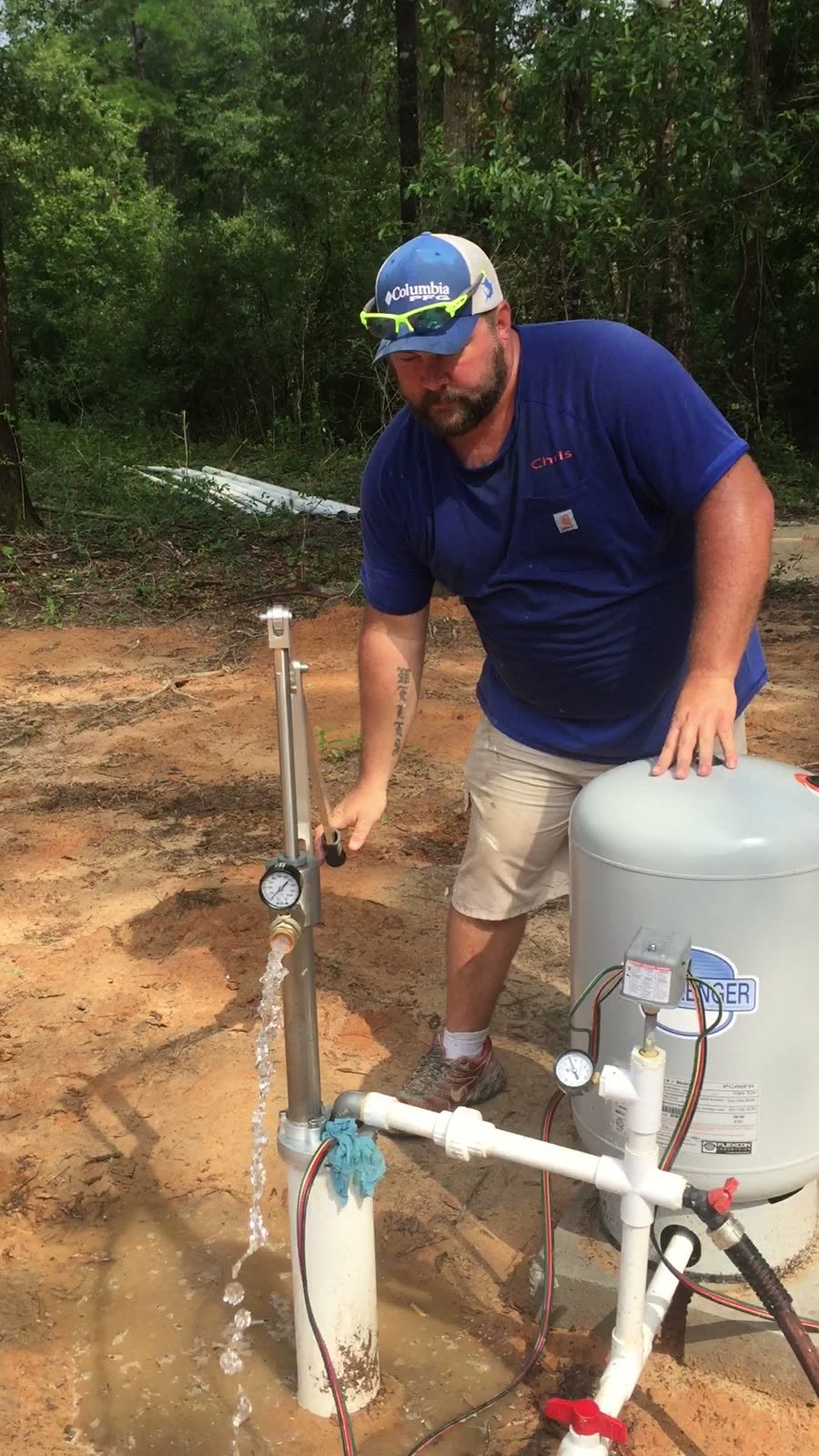 Chris working a Simple Pump hand pump at a well head, water running out