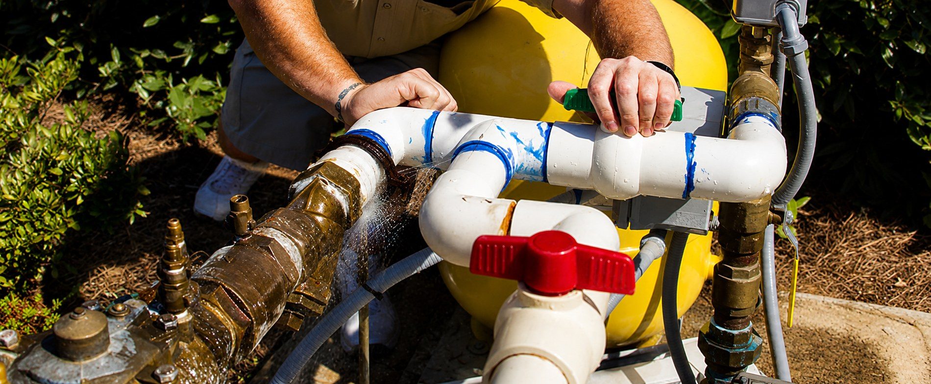 Hands at work on well pump and pressure tank plumbing