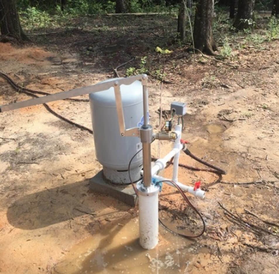 A finished H&P Wells wellhead and pressure tank set on a pad in the piney woods