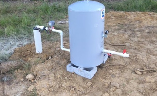 New pressure tank set on a concrete pad beside a finished well